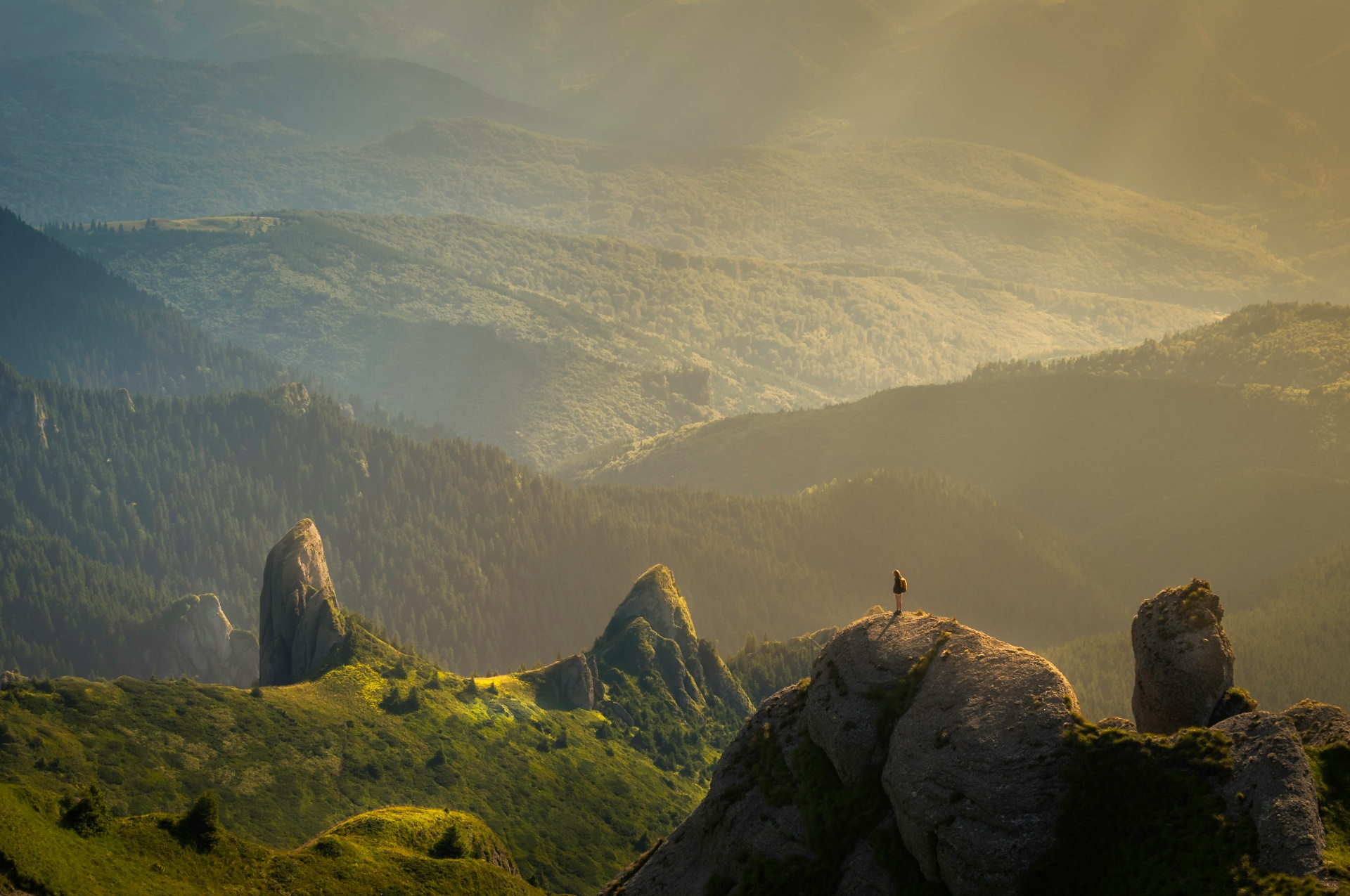 Hiker standing on a rocky outcrop overlooking misty green mountains