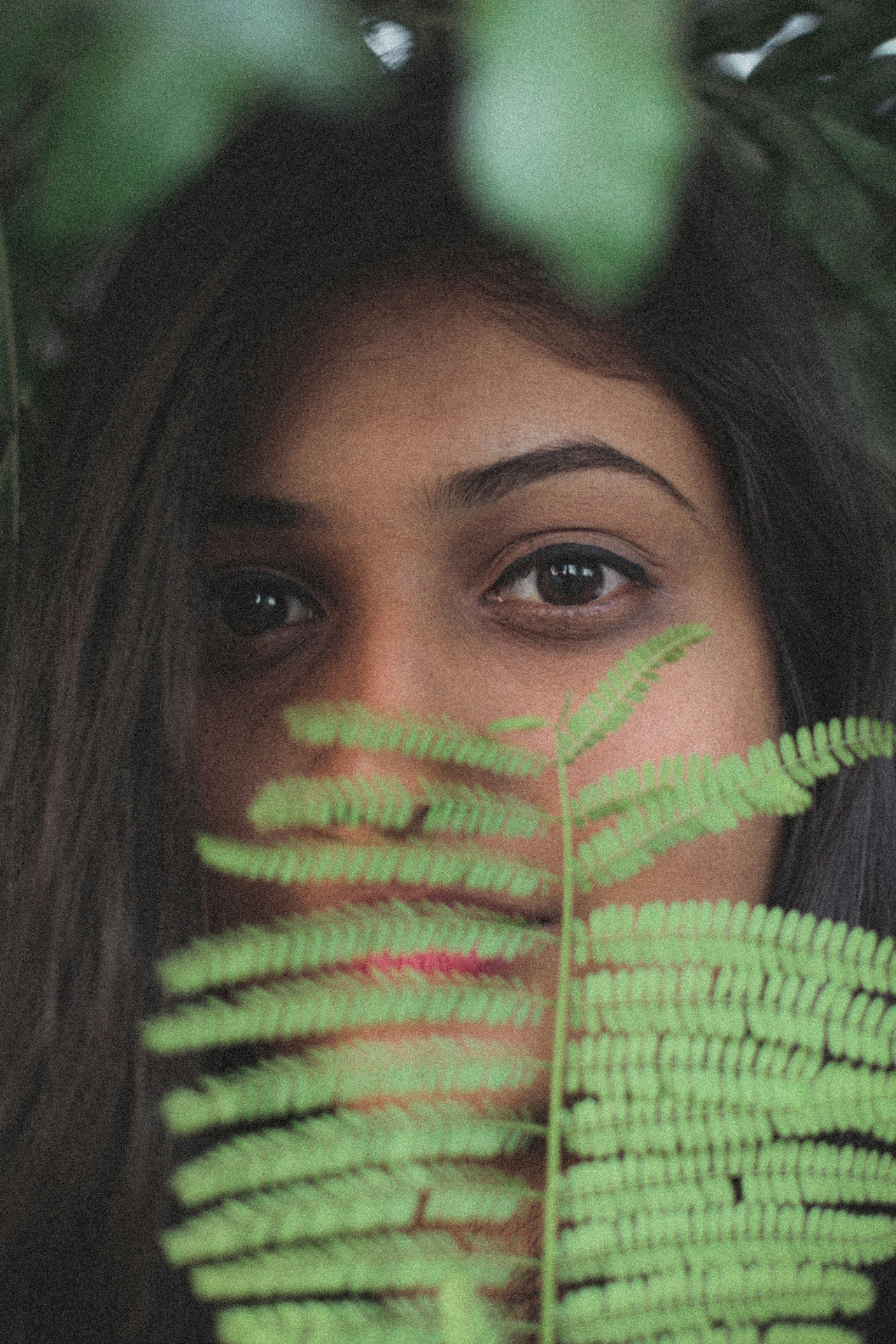 Person partially seen behind a green fern leaf